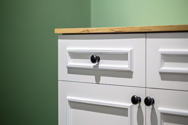 Closeup of a white cabinet with black handles on a green wall background