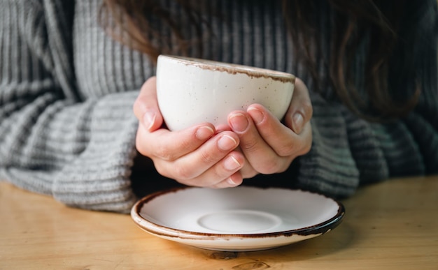 Primo piano una tazza bianca in mani femminili su uno sfondo sfocato