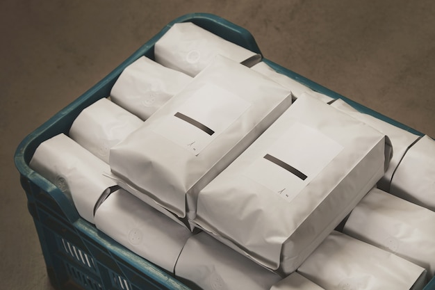 Closeup white filled with coffee or tea sealed packages in plastic box on concrete floor in warehouse.