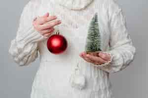 Foto gratuita primo piano di una donna bianca che tiene un minuscolo albero di natale in uno e una palla rossa nell'altra