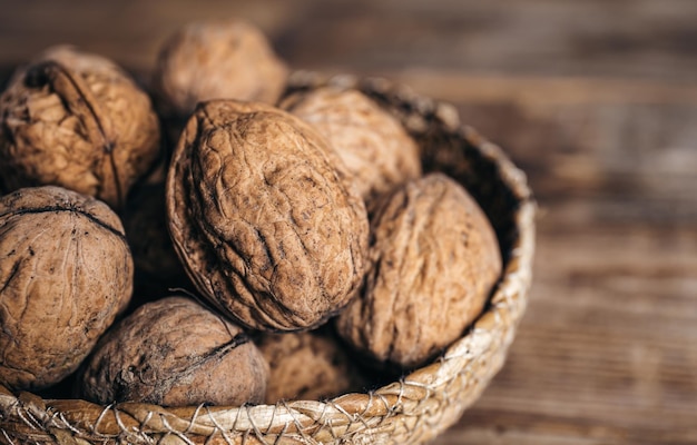 Closeup whole walnuts in a wicker bowl on a wooden background