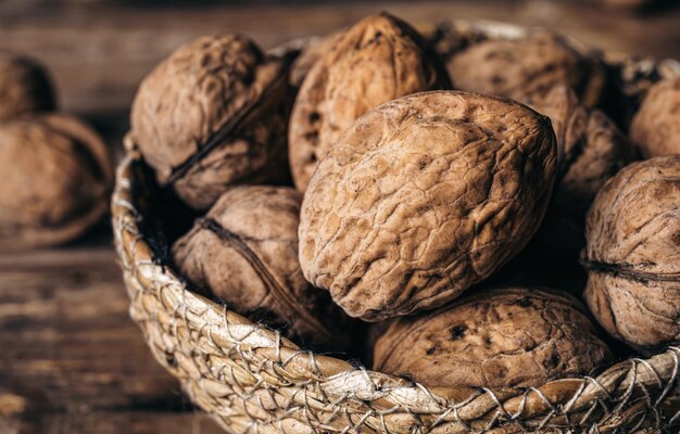 Closeup whole walnuts in a wicker bowl on a wooden background