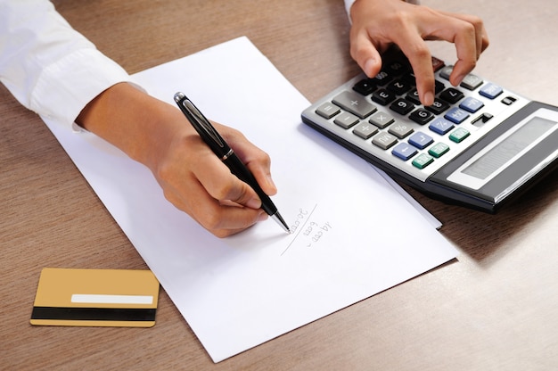 Closeup of woman calculating on calculator and writing