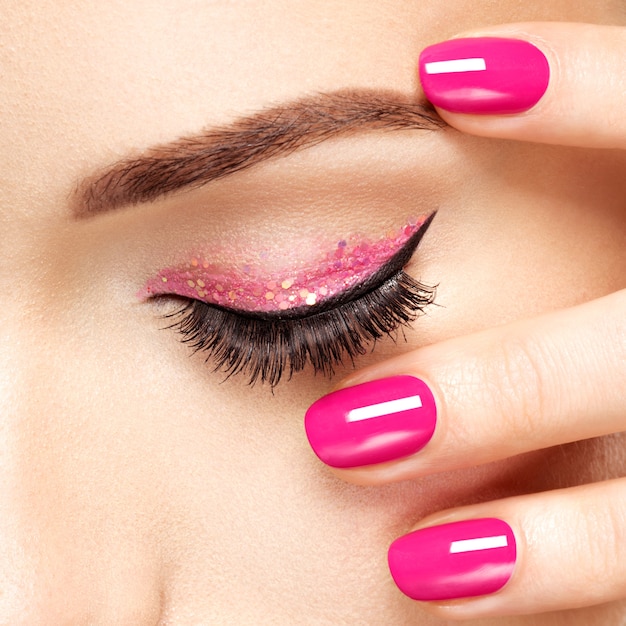 Fronte della donna del primo piano con le unghie rosa vicino agli occhi. unghie con manicure rosa