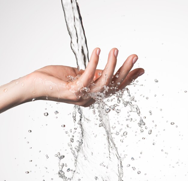 Крупным планом женская рука под струей брызг воды - концепция ухода за кожей