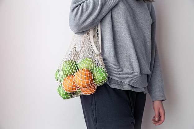 Крупным планом женщина держит авоську с яблоками и апельсинами
