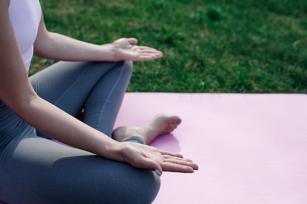 Closeup of woman open palms and young woman sitting in lotus position on sports mat in summer on gra...