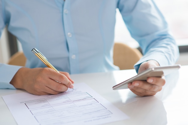 Closeup of woman signing document and holding smartphone