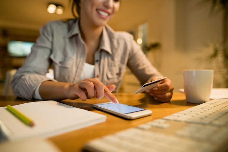 Free Photo closeup of woman sing credit card and smart phone while shopping online at night at home