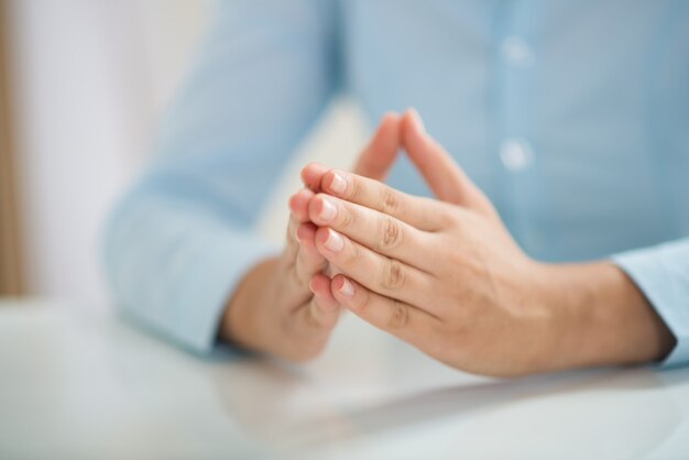 Closeup of woman sitting at table and holding hands together