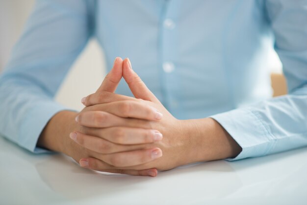 Closeup of woman sitting at table with her hands clasped