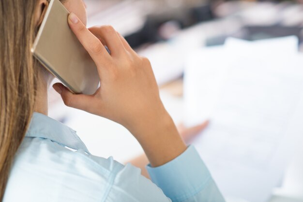 Closeup of woman talking on smartphone and holding papers