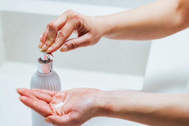 Closeup of woman using soap dispenser while washing hands in the bathroom