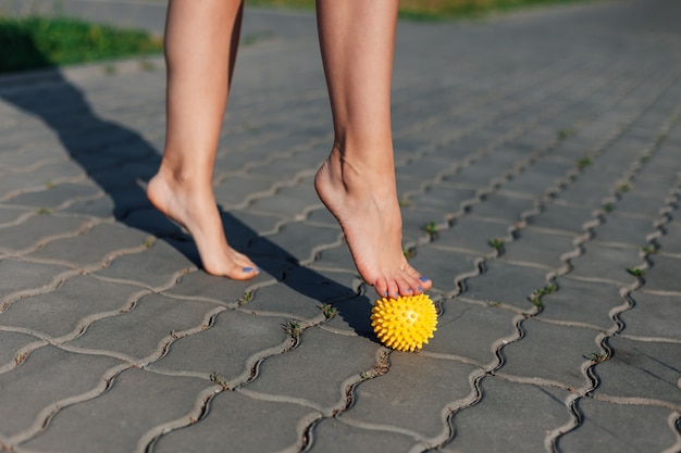 Closeup of women bare feet standing on spiked massage ball to relax or fix flat feet on paving slabs...