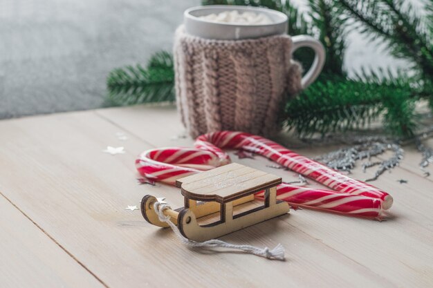 Closeup of a wooden sledge ornament with candy canes and a mug of marshmallows on the table