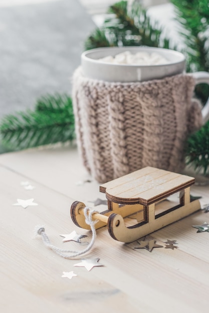 Closeup of a wooden sledge ornament with a mug of marshmallows on the wooden table