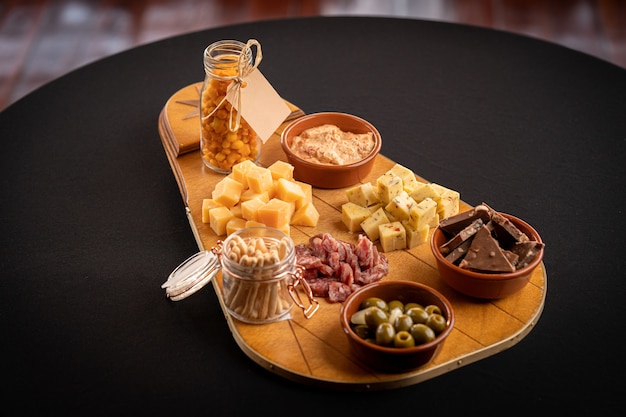 Closeup of a wooden trace with cheese assortment, green olives, chocolate bars