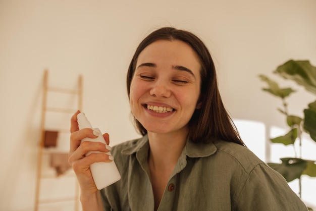 Closeup of young caucasian brunette woman holding cosmetic milk in light room Girl closes her eyes and enjoys facial treatment Wellness and self care concept