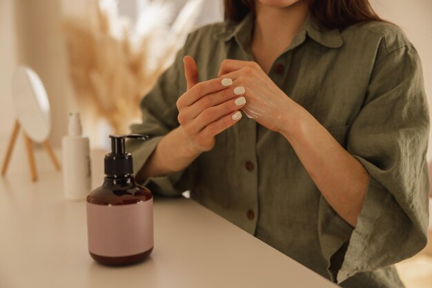 Closeup of young caucasian girl applying moisturizer on her hands while sitting at table Lady with healthy skin uses skin care cosmetics Women's beauty concept