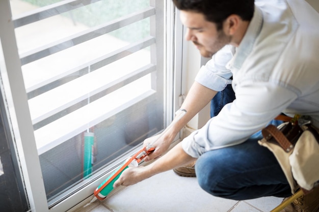 Free photo closeup of a young handyman applying some sealant on a door with a sealing gun