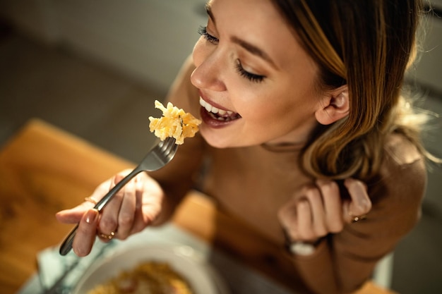 Closeup of young happy woman eating pasta at dining table