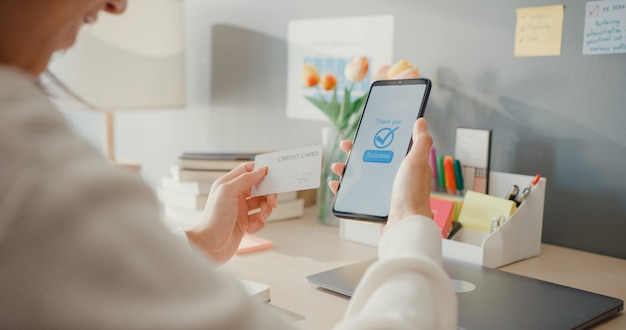 Closeup young lady use cellphone order online shopping product and pay bills with credit card in living room interior at house, 