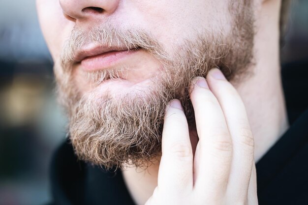 Closeup a young man touches his beard with his hand