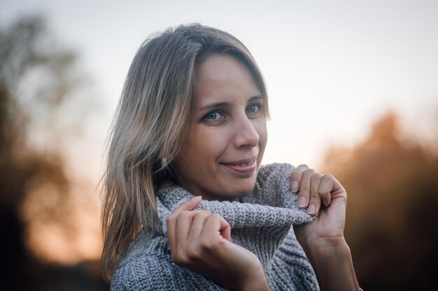 Closeup of young woman face standing in forest looking away smiling and touching sweater collar with...