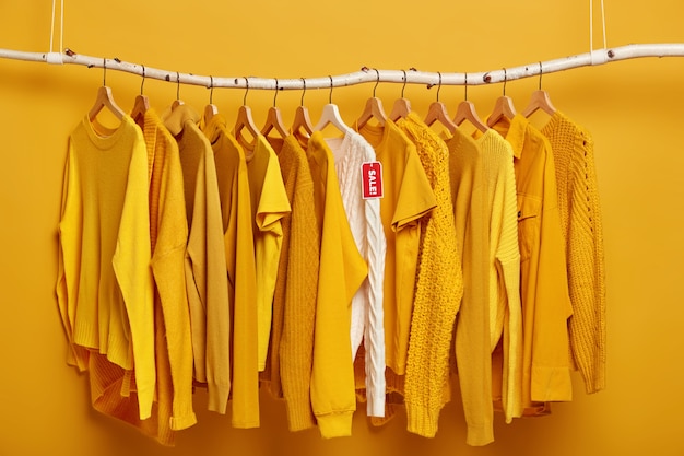 Вешалка для одежды наполнена однотонными желтыми женскими свитерами. Один белый свитер выделяется из коллекции, находясь в продаже.