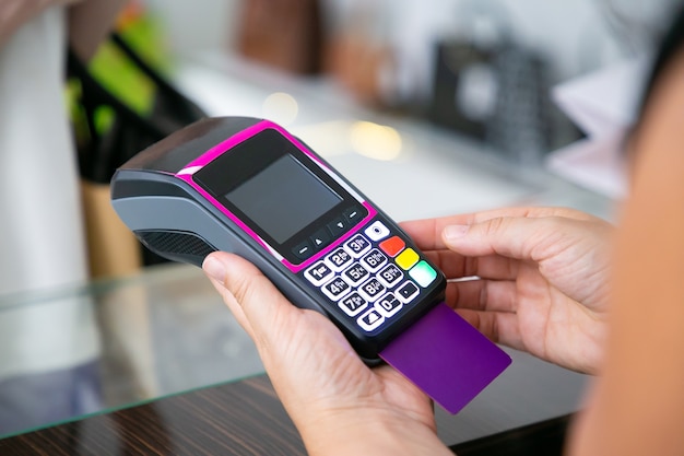 Clothes store cashier operating payment process with pos terminal and credit card. Cropped shot, closeup of hands. Shopping or purchase concept