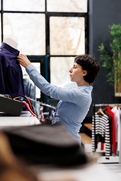 Free photo clothing store worker arranging formal shirt on mannequin, preparing boutique for customers. caucasian woman with short hair working with fashionable merchandise in shopping mall