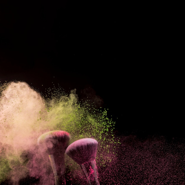 Cloud of powder and two makeup brushes at bottom on dark background