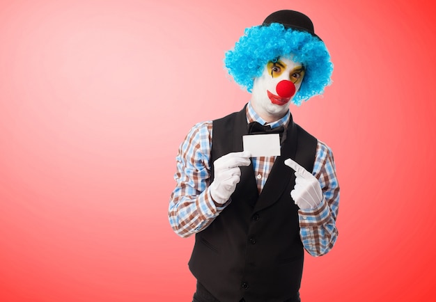 Free photo clown holding and pointing a white card