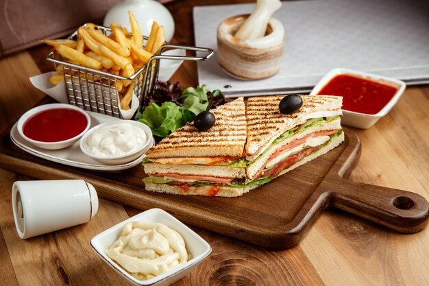 club sandwich chicken tomato lettuce ketchup mayo and french fries on board