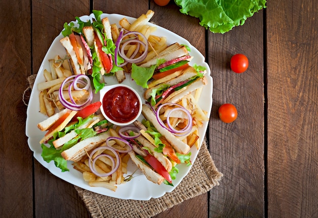 Club sandwich con formaggio, cetriolo, pomodoro, carne affumicata e salame. servito con patatine fritte.