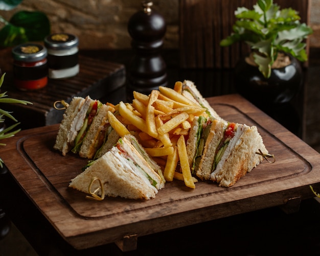 Club sandwiches with fried potatoes on a wooden board