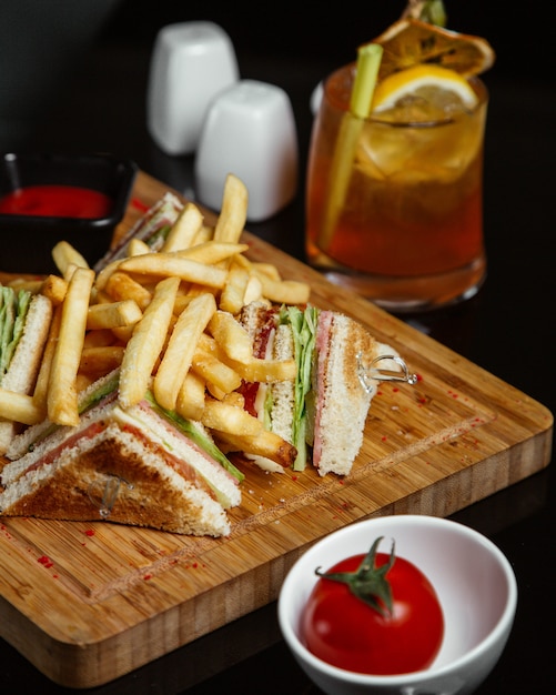 Клубные бутерброды с картофелем на деревянной доске с помидорами и лимонадом.