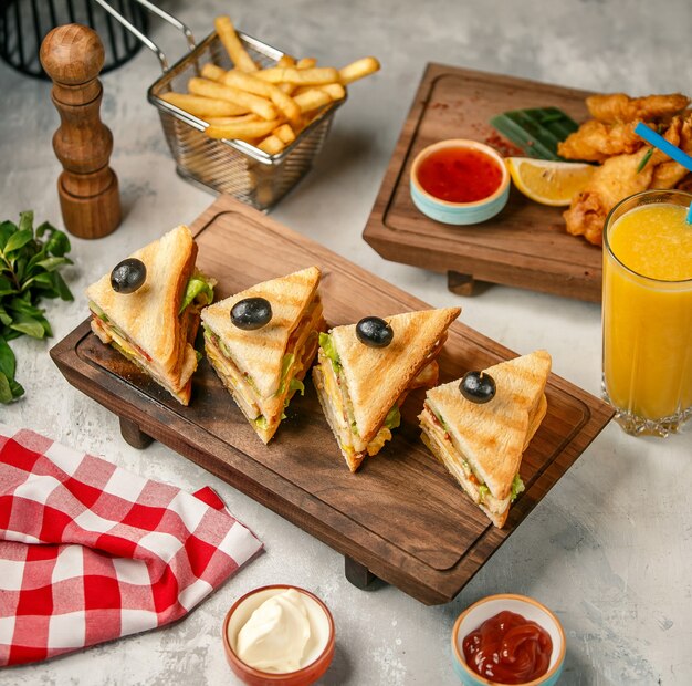 Club sandwiches on a wooden board with fries and orange juice.