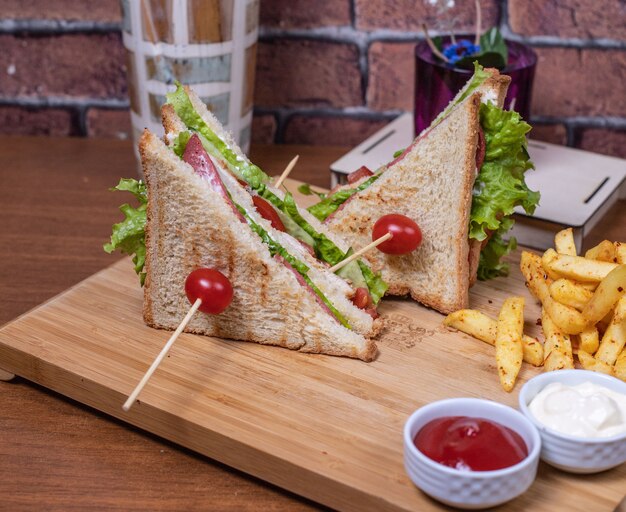 Club sandwiches on a wooden board with sauces.