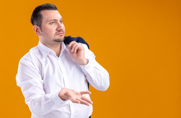 Clueless adult slavic businessman holding jacket on his shoulder looking and pointing at side with his hand