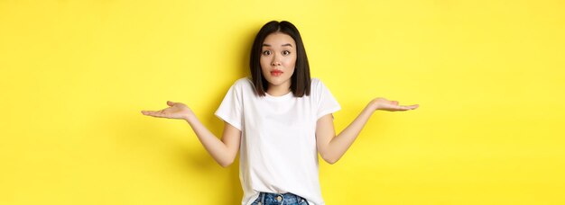 無知なアジアの女の子は肩をすくめて手を広げ、混乱しているように見え、何も立っていないことを知っています