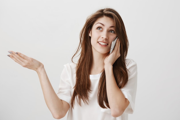 Clueless attractive woman talking on phone and shrugging indecisive