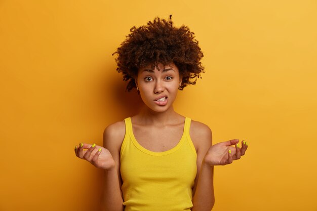 Clueless doubtful woman shrugs with spread palms, clenches teeth