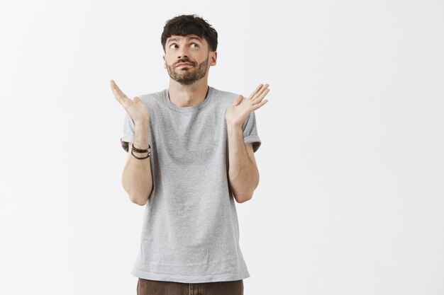 Clueless handsome guy posing against the white wall