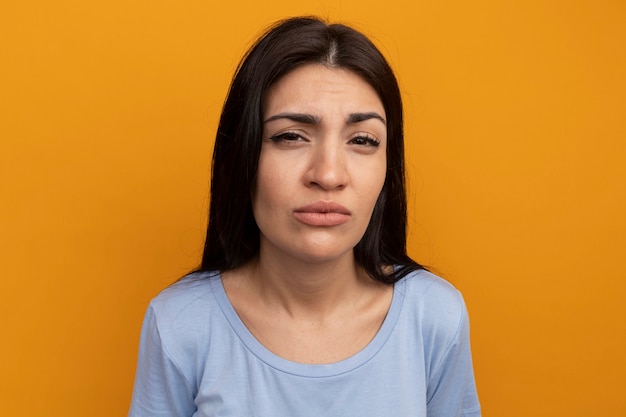 Clueless pretty brunette woman looks at front isolated on orange wall