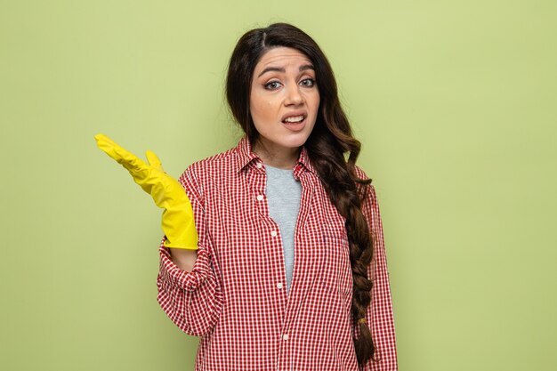 Clueless pretty caucasian cleaner woman with rubber gloves keeping hand open and looking 