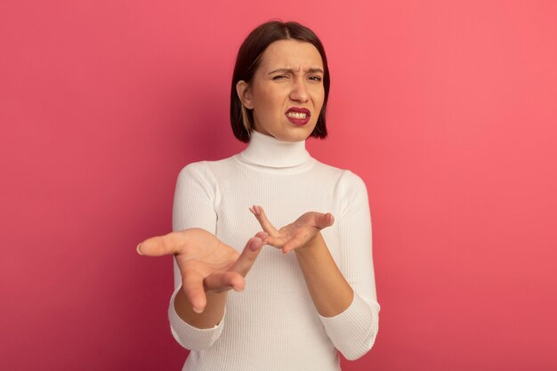 Clueless pretty woman points at front with hands isolated on pink wall