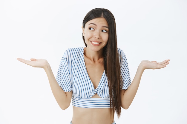 Clueless silly cute dark-haired woman in trendy cropped top shrugging with palms