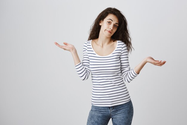 Clueless woman in striped blouse shrugging perplexed