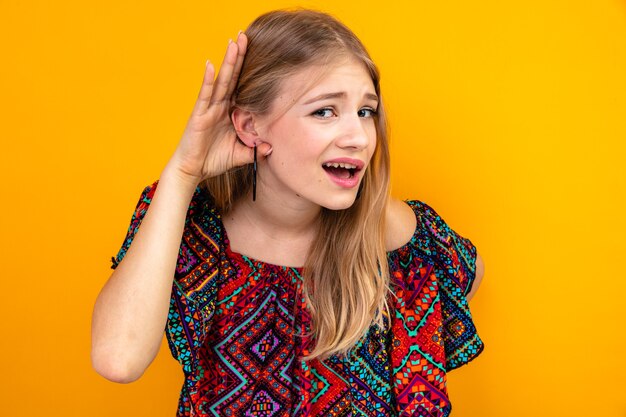 Невежественная молодая славянская блондинка держит руку рядом с ухом, пытаясь услышать